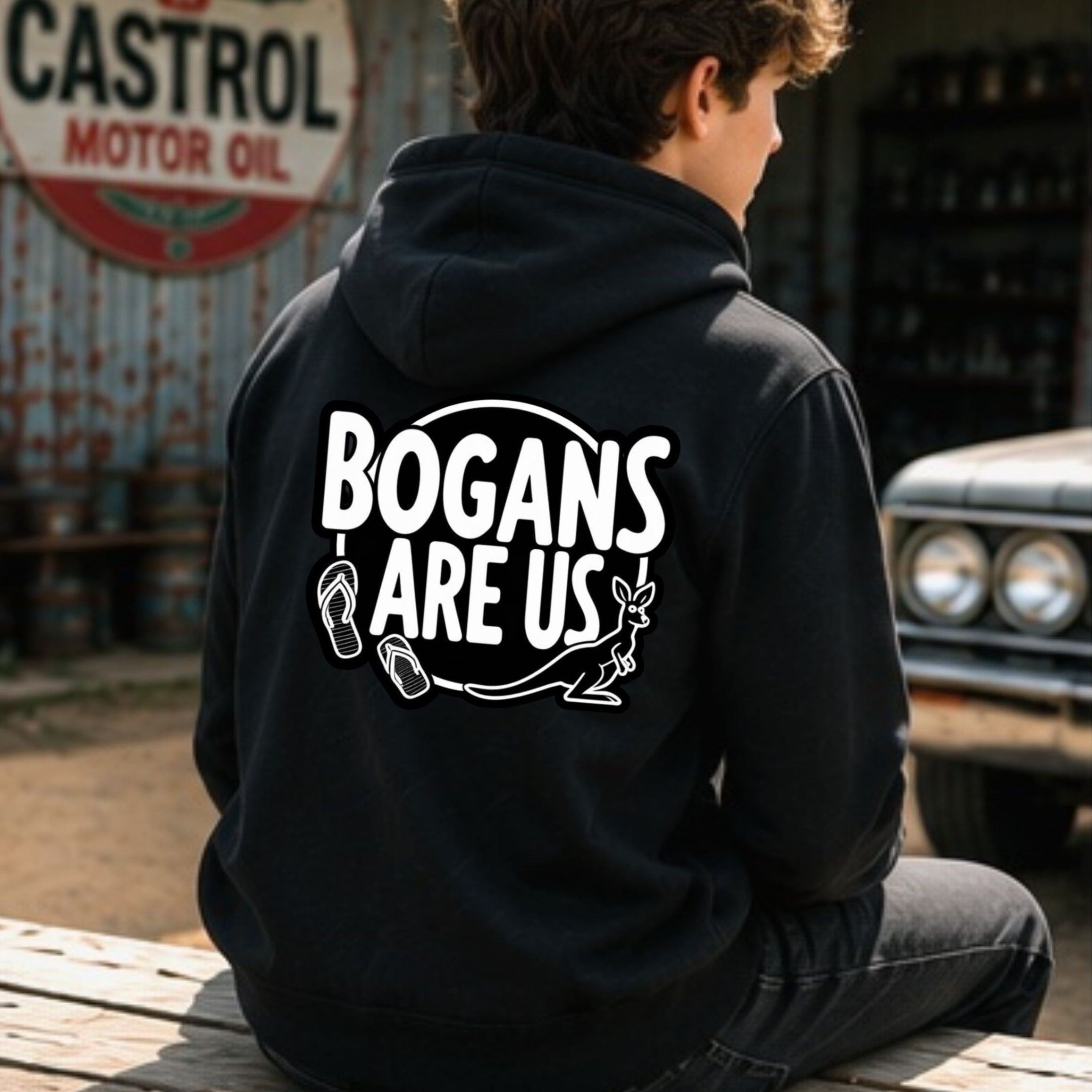 A person sitting on a wooden bench in a rustic garage setting, viewed from behind. They are wearing a black hoodie with a bold white graphic on the back that reads 'BOGANS ARE US' with a fish illustration.