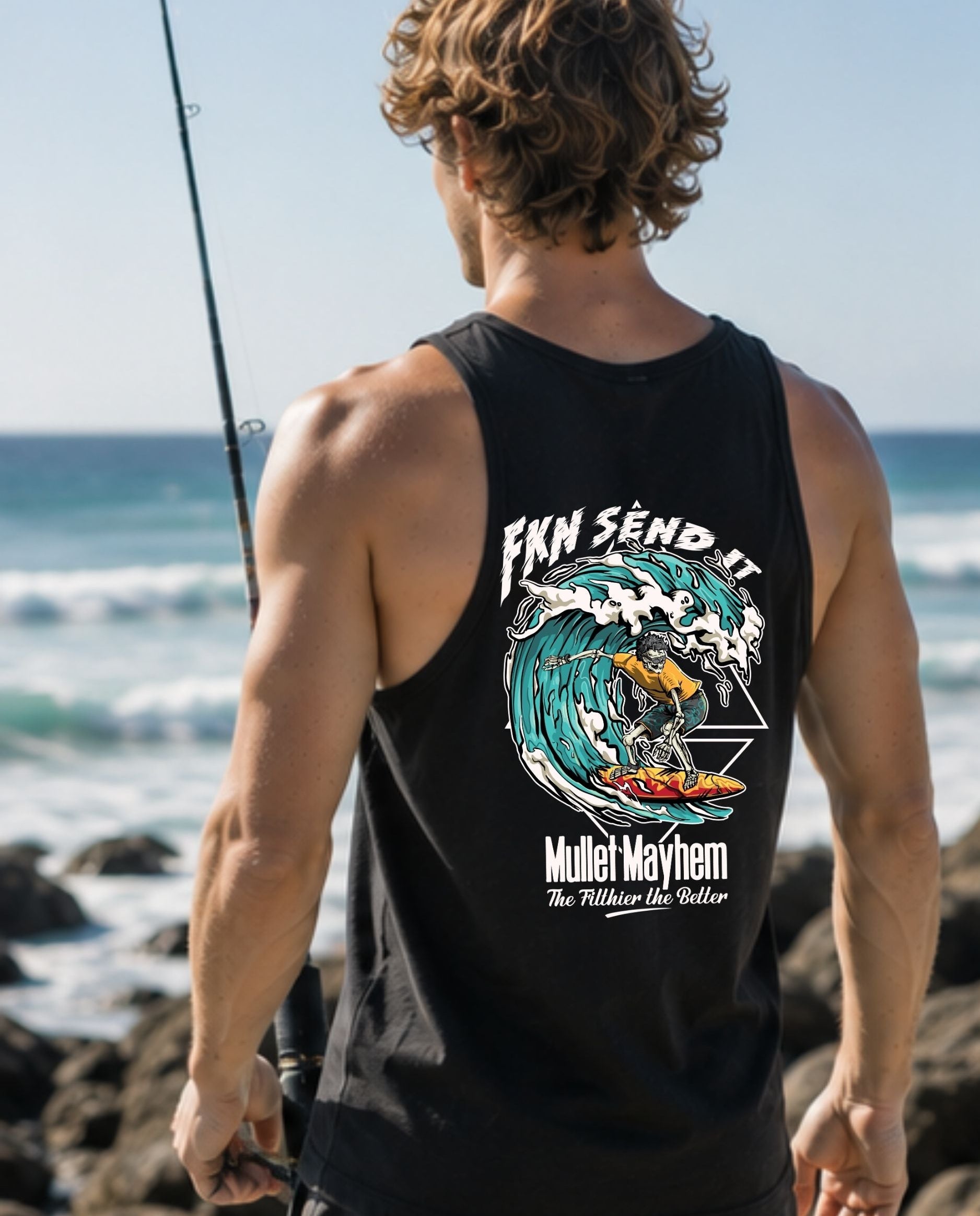 A man stands on a rocky beach facing the ocean, wearing a black tank top with a large graphic print on the back. The graphic features a wave illustration and the text 'FKN SEND IT' and 'Mufei Mayhem'.