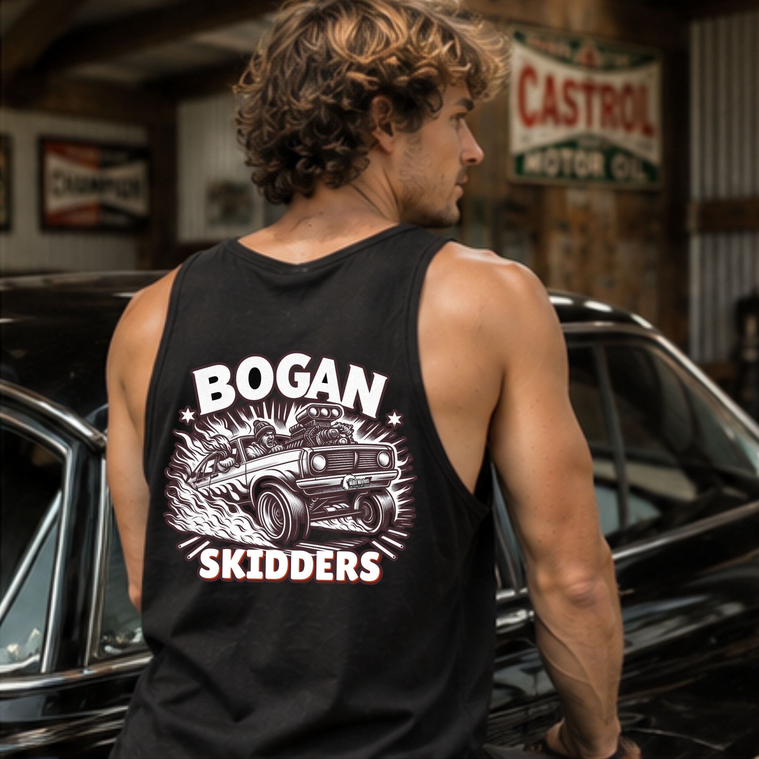 A man wearing a black tank top with a large white graphic print reading 'BOGAN SKIDDERS' and showing a vintage car illustration, standing in a garage next to a black car.